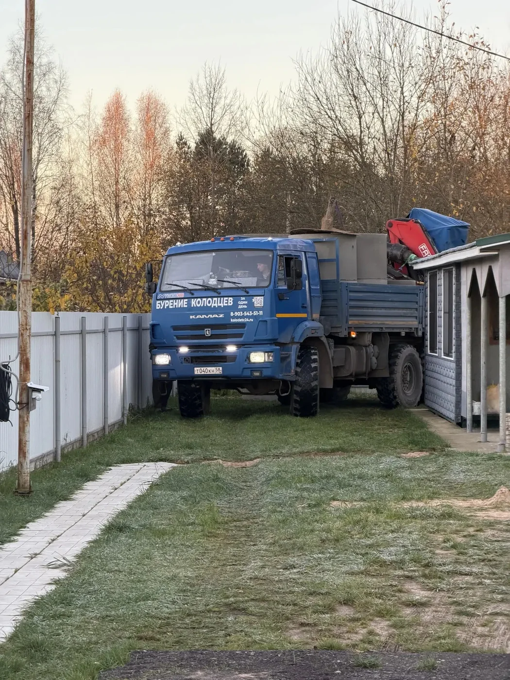 КамАЗ с надписью «Бурение колодцев» на борту у ворот участка